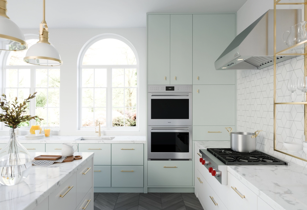 Modern kitchen with light green cabinets, marble countertops, built-in double oven, gas stove, and large arched windows letting in natural light.