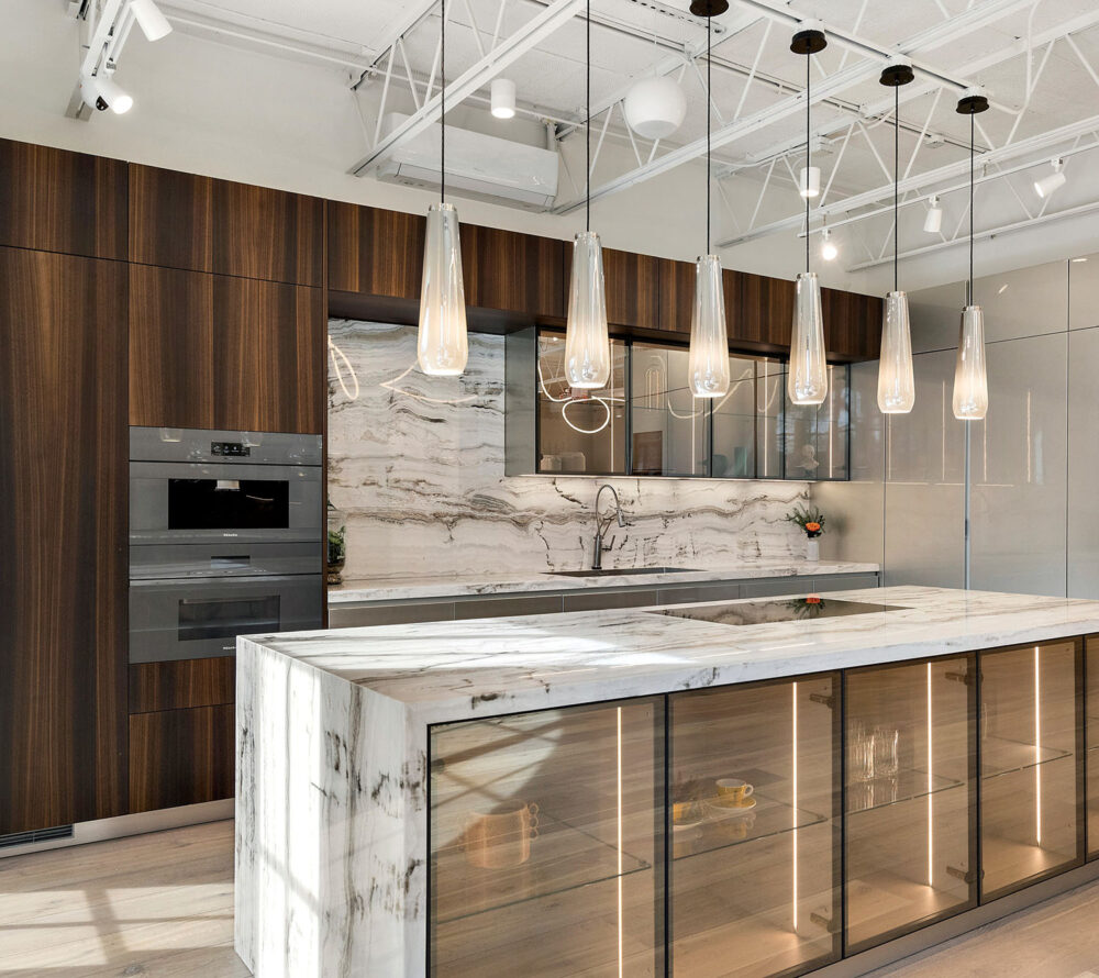 Modern kitchen with dark wood cabinets, marble countertops and backsplash, glass pendant lights, and a large island with glass-front storage.