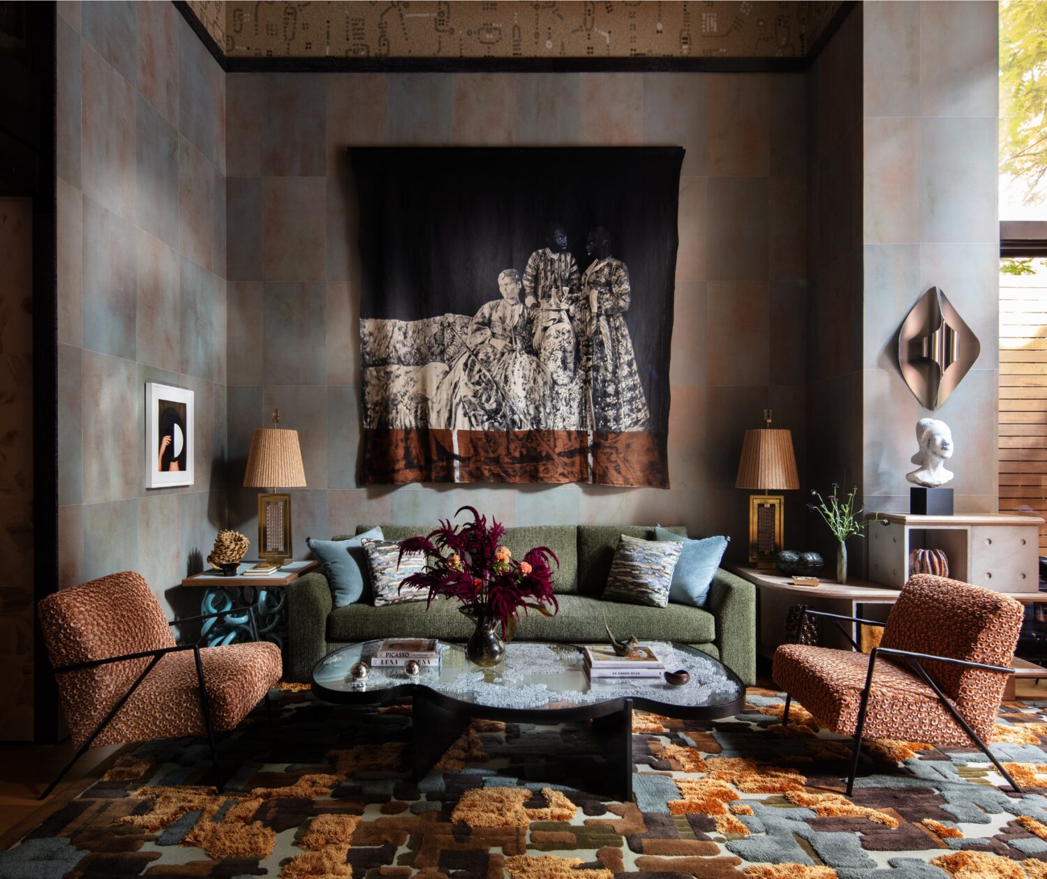 A stylish living room with a green sofa, patterned chairs, modern art, a wall tapestry, decorative lamps, and a geometric rug in earthy tones by designer Kelly Zerbini.