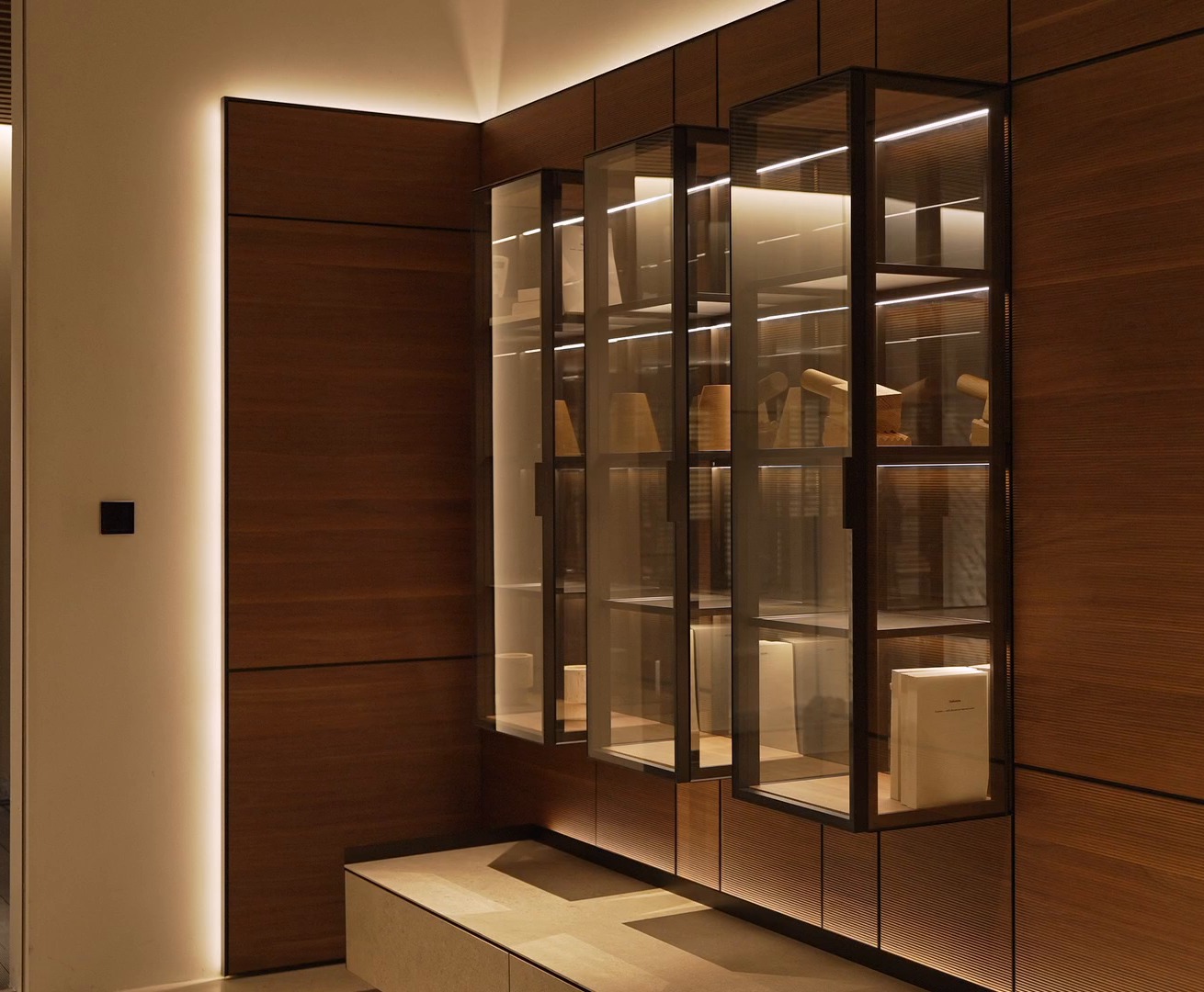 Three illuminated glass display cabinets mounted on the walnut panels of the Arundel wall system.