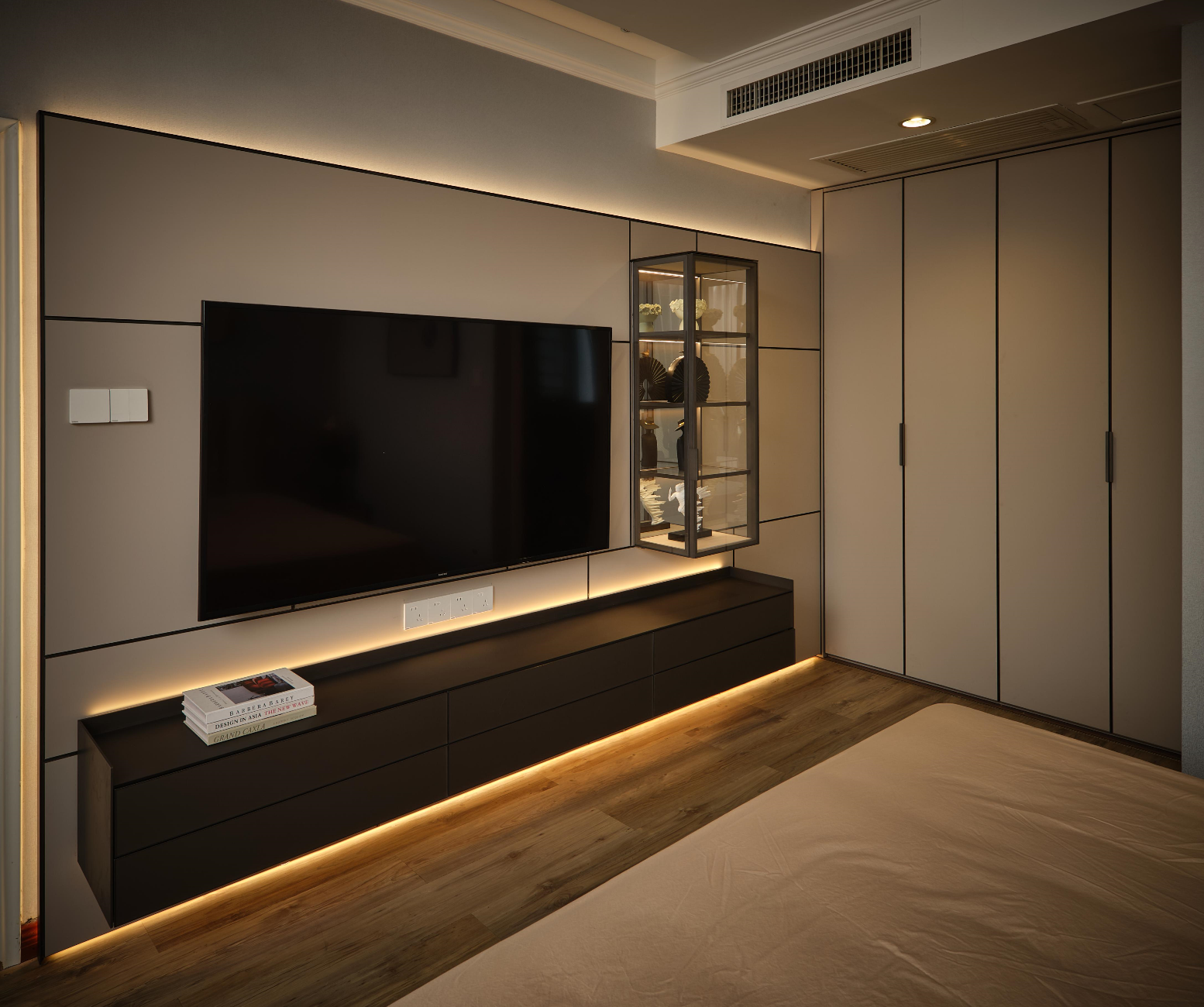 A pale-finish Arundel wall system in a bedroom, with a floating drawer console, lit panel edges, and a single glass display cabinet.