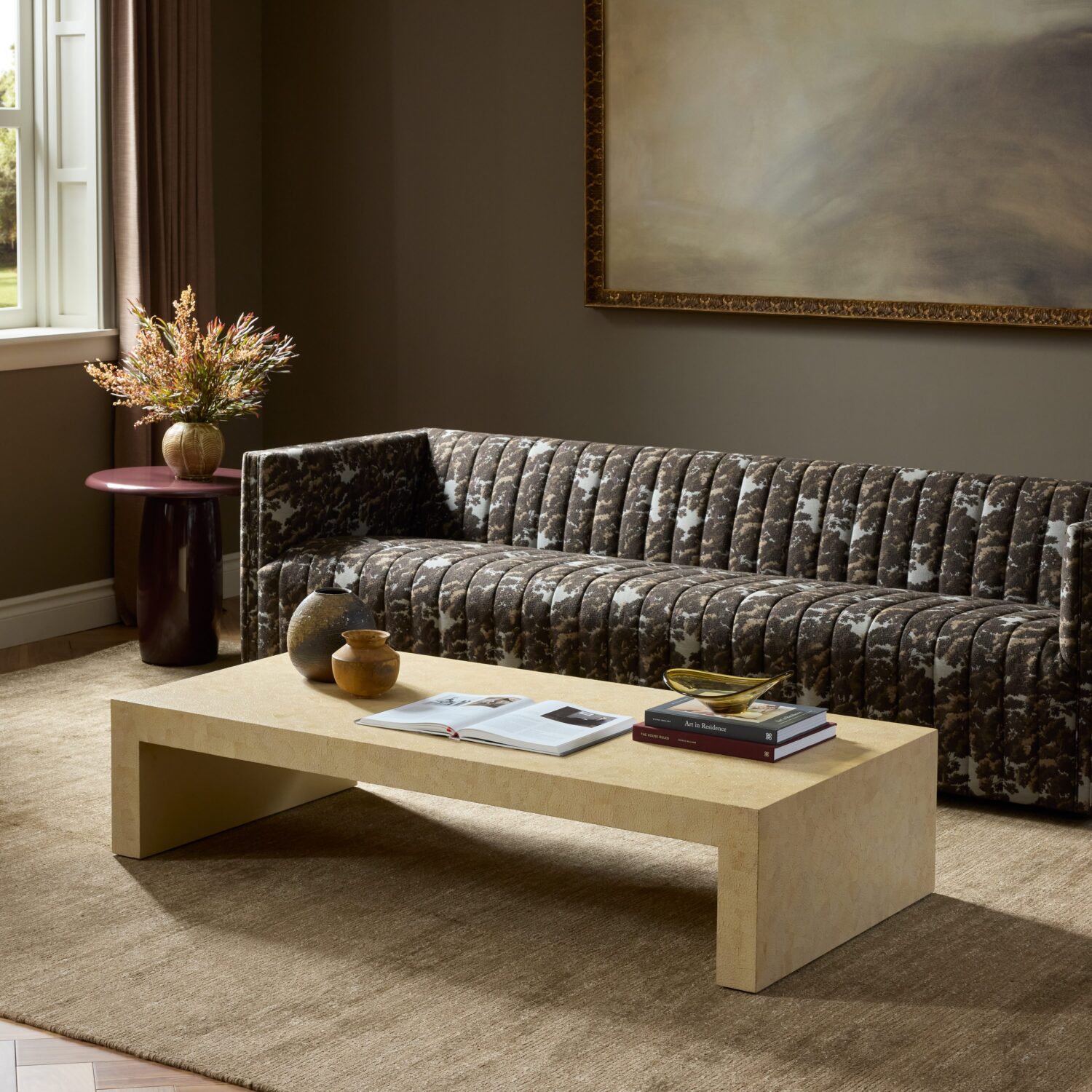 A patterned sofa sits behind a low, rectangular beige coffee table topped with two books and small decorative vessels.